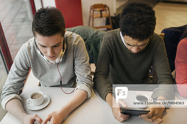 Männliche Universitätsstudenten mit digitalem Tablett am Kaffeetisch