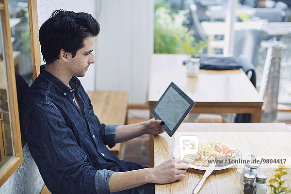 Mann mit digitalem Tablett beim Mittagessen im Cafe
