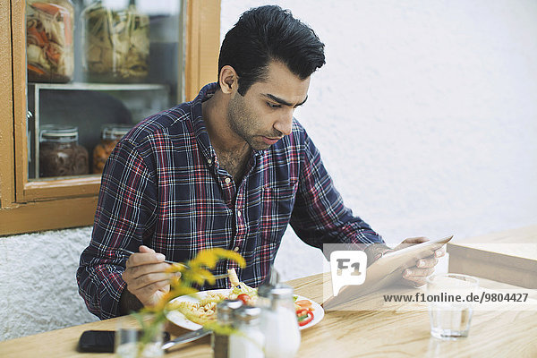 Man using digital tablet while having lunch at restaurant