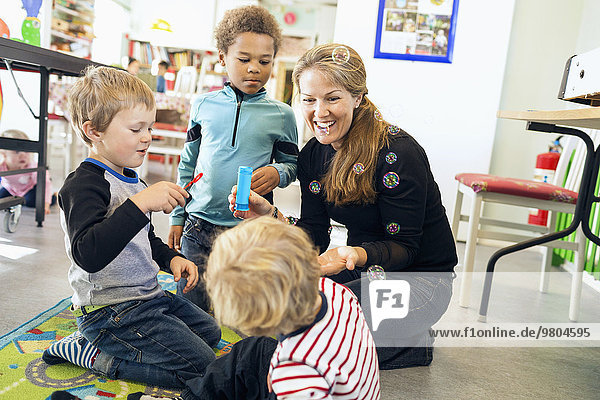 Glückliche Lehrerin und Kinder beim Blasenspiel im Kindergarten
