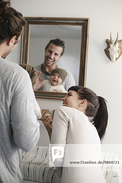 A mother and father with their baby  looking in the mirror.