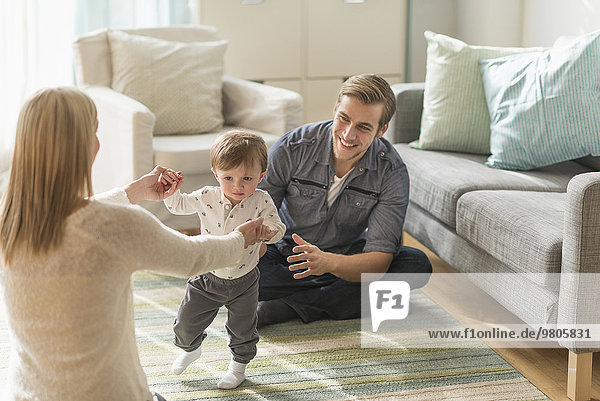 Happy parents helping little son (2-3 years) walking in living room