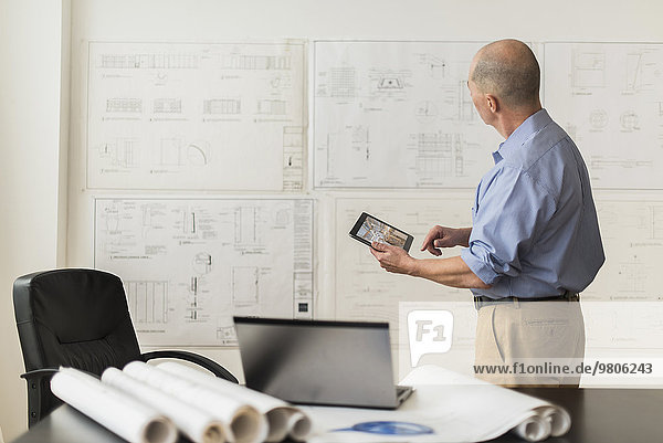 Mature architect looking at blueprints in office
