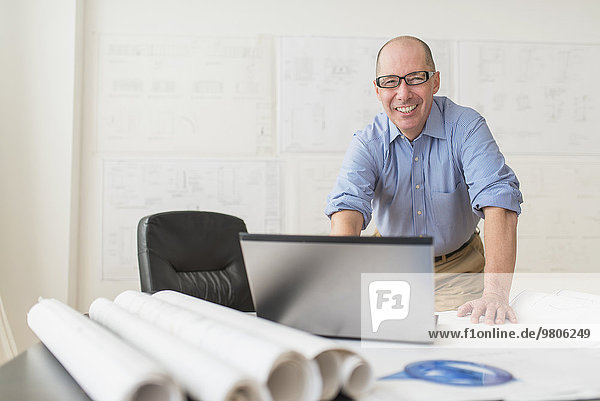 Portrait of smiling mature architect using laptop in office