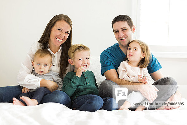 Portrait of family with three children (2-3  4-5) sitting on bed
