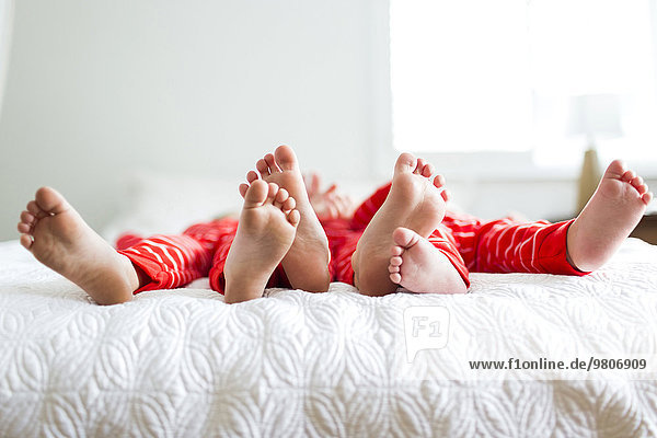 Siblings (2-3  4-5) in red pajamas lying on bed