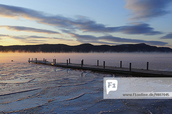 Jetty on frozen lake with vapor  hills in background at sunrise