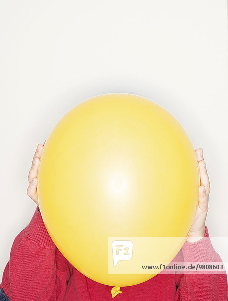 Ein Kind hält sich einen gelben Luftballon vor das Gesicht