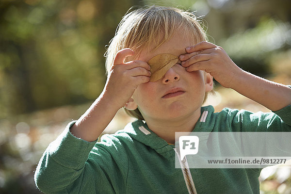 Boy holding leaf over eyes