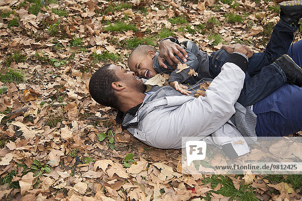 Junger Mann und Kleinkind-Sohn liegend im Herbstlaub im Park