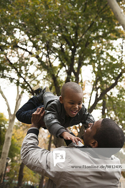 Vater hält Kleinkind-Sohn im Park hoch