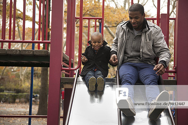 Male toddler and father side by side on park slide