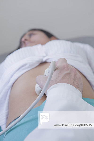 Hand des Sonographen mit Wandler auf dem Bauch der Frau