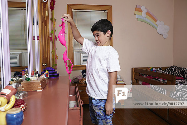 Boy holding up and staring at pink bra in bedroom