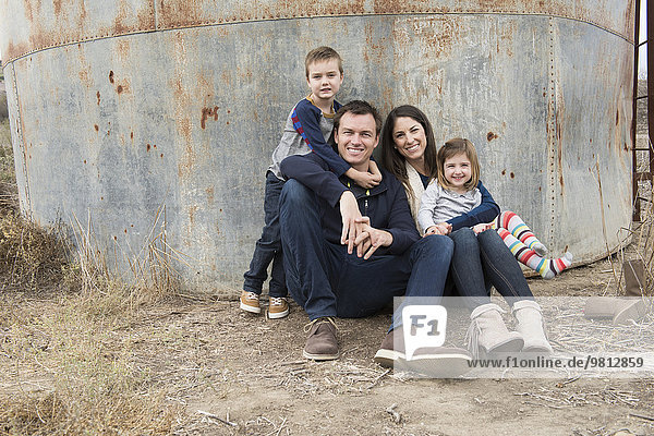 Porträt von Eltern und zwei Kindern  die sich gegen einen Eisenbehälter lehnen.