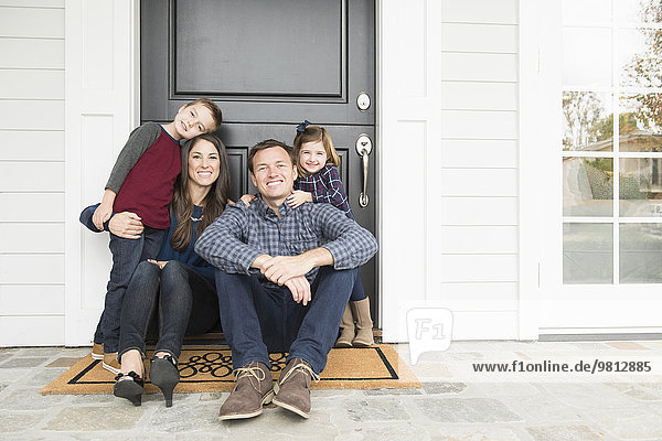 Porträt von Eltern und zwei Kindern  die vor der Haustür sitzen