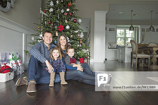 Porträt von Eltern und zwei Kindern vor dem Weihnachtsbaum sitzend