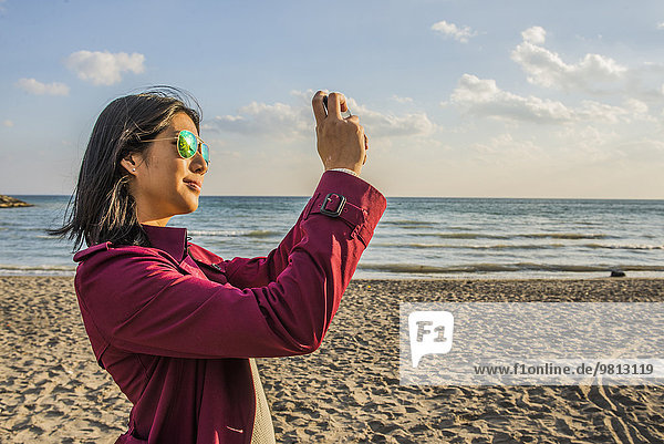 Mittlere erwachsene Frau am Strand beim Fotografieren