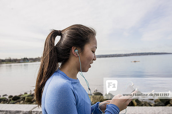 Young woman wearing headphones and holding mp3 player  English bay  Vancouver  Canada