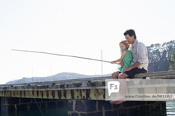 Erwachsener Mann und Tochter beim Fischen am Pier,  Neuseeland