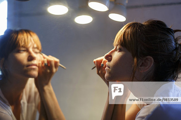 Mid adult woman applying eyeliner in bathroom mirror
