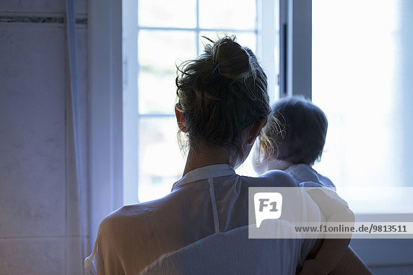 Rückansicht der mittleren erwachsenen Frau und der kleinen Tochter mit Blick aus dem Wohnzimmerfenster