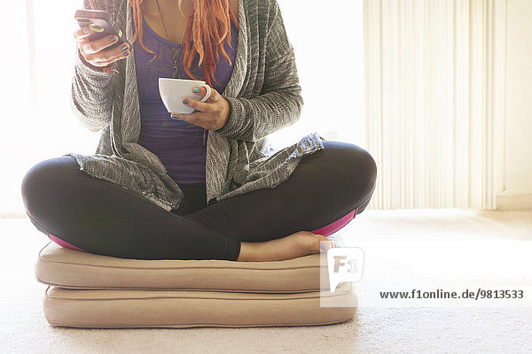 Cropped shot of young woman sitting cross legged on cushions texting on smartphone