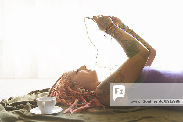 Young woman with pink dreadlocks choosing music on smartphone
