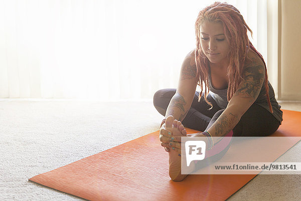 Young woman with pink dreadlocks practicing yoga on yoga mat