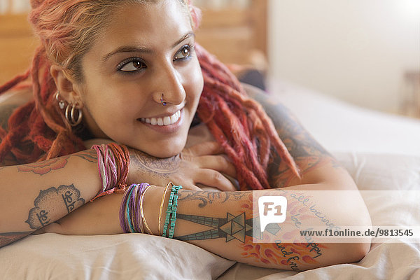Portrait of young woman with pink dreadlocks lying on bed