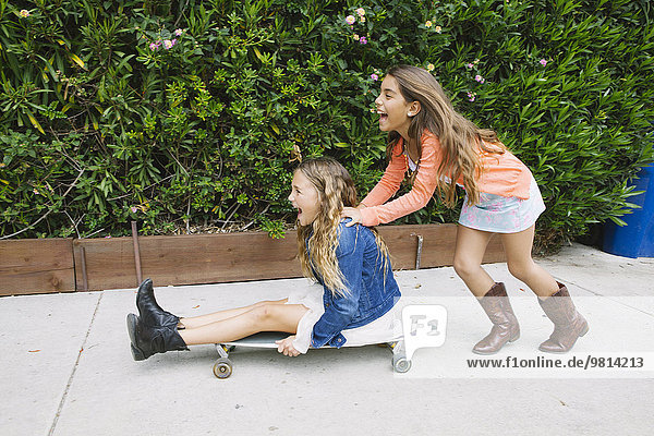 Girl pushing friend on skateboard