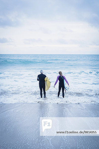 Vater und Tochter mit Surfbrettern im Meer