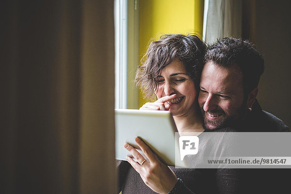 Couple standing beside window  using digital tablet