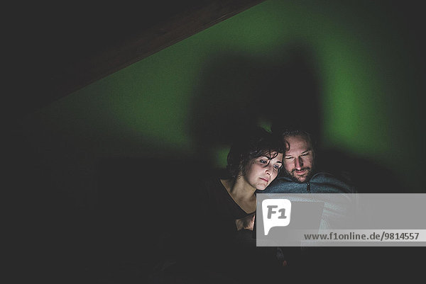 Paar sitzt in einem dunklen Raum und schaut auf ein digitales Tablett.