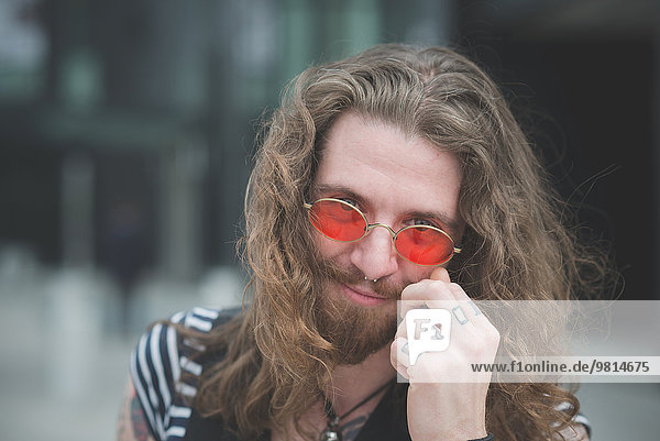 Portrait of young male hippy with orange sunglasses and tattooed fingers