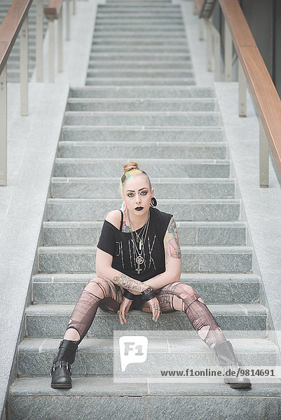 Porträt einer jungen Punkerin,  die auf einer U-Bahn-Treppe sitzt.