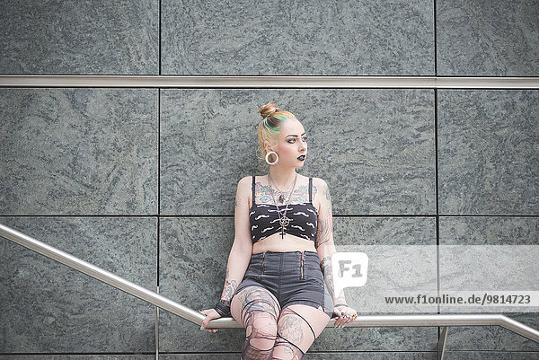 Porträt einer jungen tätowierten Punkerin auf einem U-Bahn-Geländer sitzend