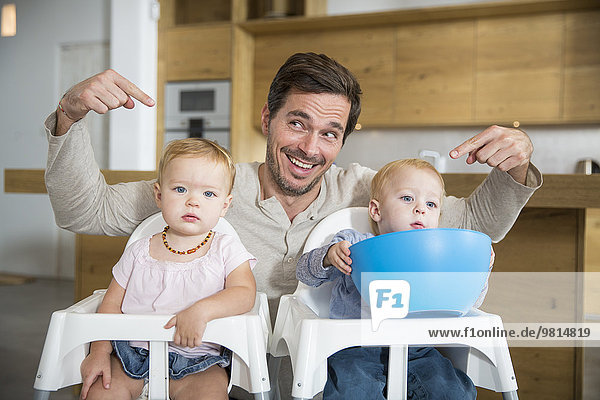Father pointing at male and female twin toddlers in high chairs
