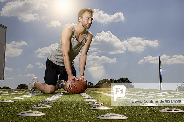 Young male basketball player exercising with ball on sports field