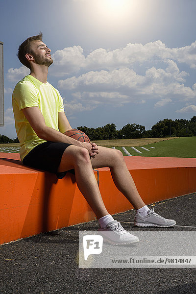 Young male basketball player sitting on wall taking a break