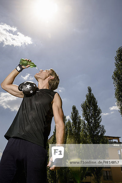 Mittlerer Erwachsener männlicher Boxer trinkt Wasser in Flaschen im Park