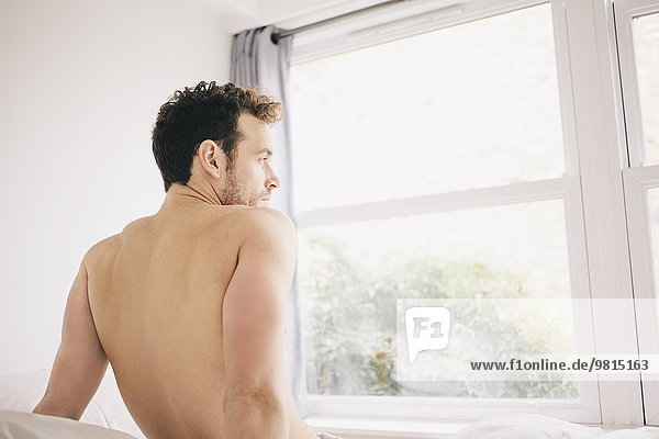 Young man looking out of bedroom window in morning