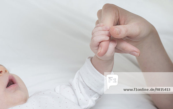 Baby girl holding mother's finger on bed