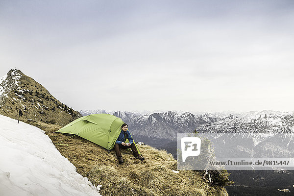 Young male hiker in front of tent on peak of Klammspitze mountain  Oberammergau  Bavaria  Germany
