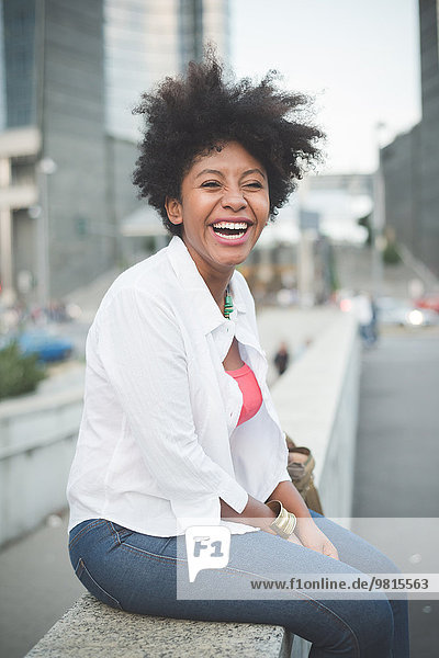 Lächelnde junge Frau sitzt auf der Wand des Einkaufszentrums