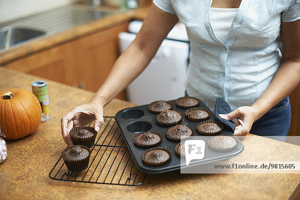Womans hands lifting cup cakes onto cooling rack