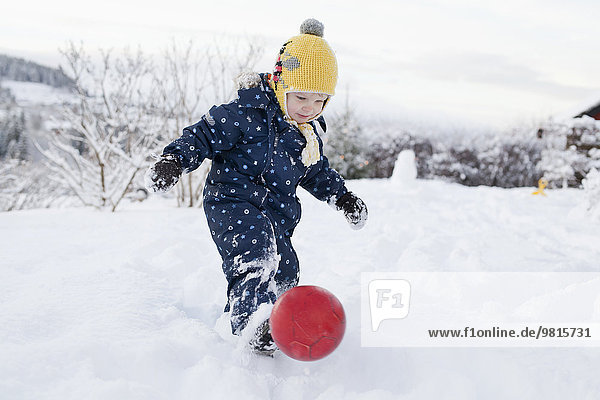 Junge tritt seinen Ball in den Schnee
