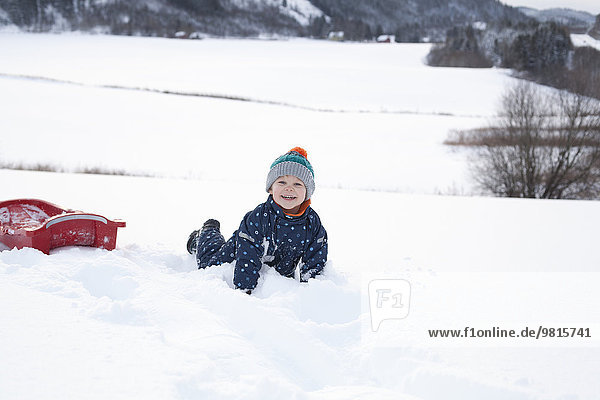 Junge spielt auf seinem Schlitten im Schnee