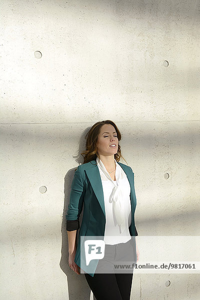 Businesswoman leaning against concrete wall