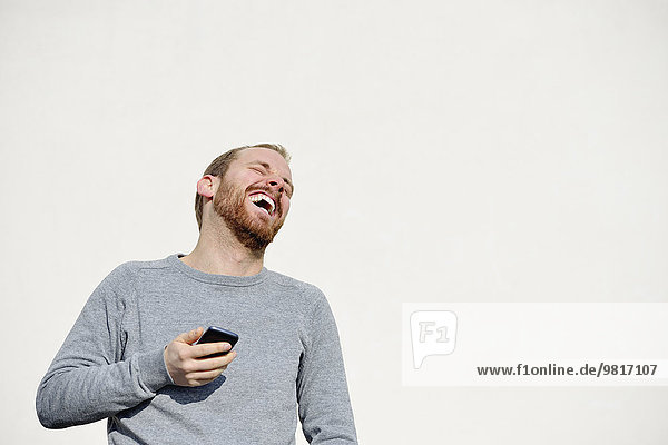 Portrait of laughing young man with smartphone in front of white background